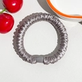 Close-up of silver-grey silk scrunchie with pleated texture on white leather background - Silk Pleated Hair Band - Silver Gray