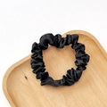 Close-up of a black satin scrunchie on a heart-shaped wooden tray with elegant folds - Black