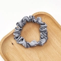 Detailed close-up of a grey pleated satin scrunchie on a wooden tray with a white backdrop - Blue Grey