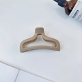 Macro shot of large matte cream hair claw clip with cutout fishtail design on white desk - Nude
