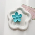 Detailed view of a matte teal flower hair claw clip resting in a white petal-shaped plate - Lake Blue