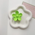 Macro shot of a matte neon green flower hair claw on a white ceramic decorative plate - Grass Green