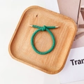 Détail d'un élastique à cheveux vert torsadé avec boucle en métal doré sur plateau en bois - Vert Lumineux