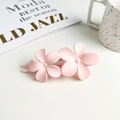Close-up of pink matte double flower hair clip next to a ceramic cup on a white table - Pink