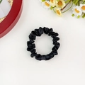 Detail shot of black satin scrunchie with silky folds on a white surface with daisy - Black