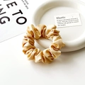 Dettaglio scrunchie in raso champagne con ciondolo logo dorato su piatto ceramica - Oro