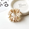 Dettaglio di scrunchie in seta champagne con ciondolo dorato su un piatto bianco decorativo - Beige