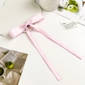 Detail of light pink satin bow hair clip with long flowing ribbons on white table - Pink