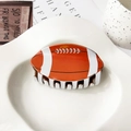 Detalle de una pinza para el cabello con forma de balón de fútbol americano en bandeja blanca - 9cm / Rugby Naranja