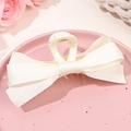 Vue détaillée d'une pince à cheveux à double nœud crème sur un plateau décoratif rose - Blanc Lait Beige