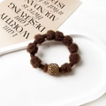 Close-up of brown plush hair tie with rhinestone gold bead on elegant white tray - Spherical / Brown