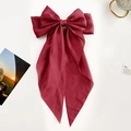 Detail of oversized burgundy satin bow hair clip with long ribbons and silky texture - Burgundy