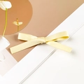 Dettaglio di un fermaglio a fiocco giallo brillante in nastro satinato con trama intrecciata - Stile Singolo / Giallo Latte