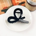 Close-up of a glossy black hair claw clip with a twisted design on a white ceramic plate - Glossy Black