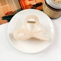 Chic beige bow hair claw clip displayed on a ceramic tray with a scented candle - Jelly Light Orange