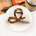 Detail view of a glossy amber tortoiseshell hair claw clip on a white ceramic plate - Amber Brown
