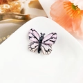 Détail macro d'une pince à cheveux papillon rose avec textures noires sur un plateau blanc - Résine Mixte / Rayures Rose Clair