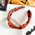 Detail eines orangen Halloween-Stirnbands mit Kürbis- und Fledermausmuster auf Keramikteller - Orange Kürbis Netz