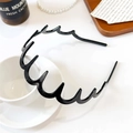 Dettaglio di un cerchietto nero ondulato su un vassoio con accessori dallo stile elegante - Cerchietto a Onda Premium / Nero Lucido