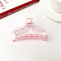 Gros plan d'une pince à cheveux en résine rose transparente avec ressort métallique - Rose transparent