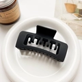Close-up of a large matte black hair claw clip displayed on a clean white ceramic plate - Matte Black