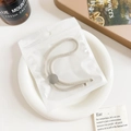 Detail of cream elastic hair tie with silver button in clear polybag on ceramic plate - Plastic/Resin / Basic Adjustable Hair Tie - Silver Buckle Beige
