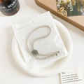 Close-up of adjustable threaded hair tie with textured silver metal disc in packaging - Plastic/Resin / Basic Adjustable Hair Tie - Gray Buckle Beige