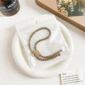 Detailed close-up of khaki ribbed elastic hair tie with textured gold metal buckle in packaging - Plastic/Resin / Threaded Adjustable Hair Tie - Gold Buckle Coffee