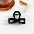 Close-up of a glossy black bow-shaped hair claw clip on vintage book pages - 8cm Hollow Bowknot / Glossy Black