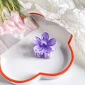 Detail view of a purple resin plumeria hair claw clip on a decorative white ceramic plate - Flower / 4cm / Gradient Lavender
