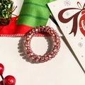 Close-up of a festive red spiral hair tie featuring Santa, trees, and snowflake patterns - Red