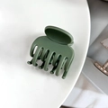 Détail d'une pince à cheveux vert olive mat à sept dents sur un socle blanc pur - Vert olive