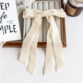 Detailed view of off-white velvet bow hair clip on a wooden display tray with vintage candle - Beige