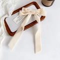 Close-up of cream velvet bow hair clip with long ribbons on a decorative wooden tray - Beige