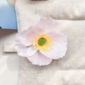 Gros plan d'une pince à cheveux fleur de frangipanier rose sur tissu matelassé beige - Coquelicot Rose Clair