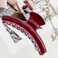 Macro di una molletta per capelli curva rosso scuro lucida su sfondo di una rivista - Rosso Vino Lucido