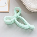 Detail of mint green marble bow hair claw clip showing acetate texture and metal spring - Cyan