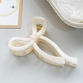 Detail of a creamy white bow hair claw clip with marble texture and gold spring - Light Orange