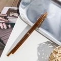 Close-up of a glossy translucent brown acrylic hair clip on a minimalist white leather surface - Linear Style / Jelly Coffee
