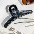 Detailed close-up of a glossy black hair claw clip with silver spring on notebook paper - Black