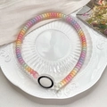 Detail of colorful spiral hair tie with round charm on white porcelain plate - Dark Rainbow Gradient