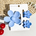 Close-up of three matte blue flower hair claws in different sizes on a display card - Matte Sky Blue