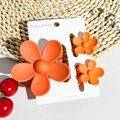 Detailed macro of three orange matte flower hair claws on a fashion display card - Matte Orange Red