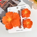Detailed view of orange plumeria hair clips set on display card with soft floral textures - Hibiscus Triple Clip Set - Gradient Orange