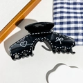 Détail d'une pince à cheveux noire avec motifs cœurs et nœuds sur plateau blanc - Style d'Arche Noir