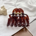 Detail of large brown translucent hair claw clip with golden spring on white textured fabric - UV Transparent Amber