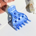 Vista dettagliata del fermaglio per capelli marmorizzato blu con design a fori su base bianca - Celeste