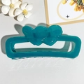 Detail view of a teal jelly hollow heart-shaped hair claw clip on white leather - Transparent Peacock Blue