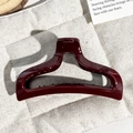 Close-up of a burgundy fishtail hair claw clip made of glossy acrylic on a wooden tray - Burgundy