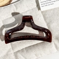 Detailed view of dark brown tortoiseshell hair claw clip on quilted beige fabric - Transparent Amber